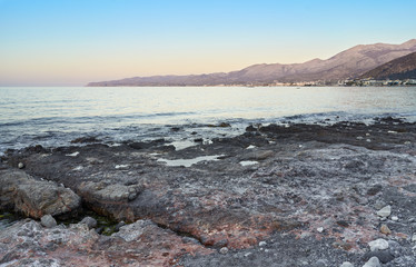 Beautiful summer sunrise on Greek island Crete. Stone beach, little town  and mountains in background.