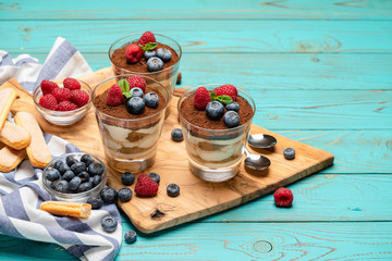 Classic tiramisu dessert with blueberries and strawberries in a glass cup and savoiardi cookies on wooden background