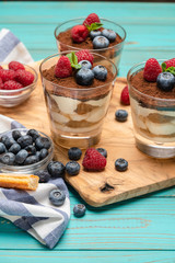 Classic tiramisu dessert with blueberries and strawberries in a glass cup and savoiardi cookies on wooden background