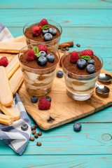 Classic tiramisu dessert with blueberries and strawberries in a glass cup and savoiardi cookies on wooden background