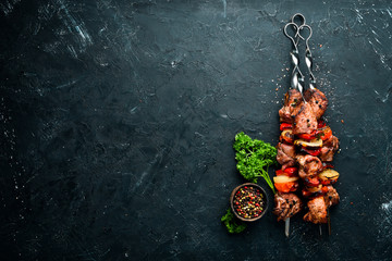 Shish kebab BBQ meat with onions and tomatoes. On a black background. Top view. Free space for your...