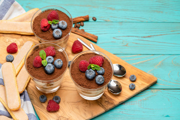 Classic tiramisu dessert with blueberries and strawberries in a glass cup and savoiardi cookies on wooden background