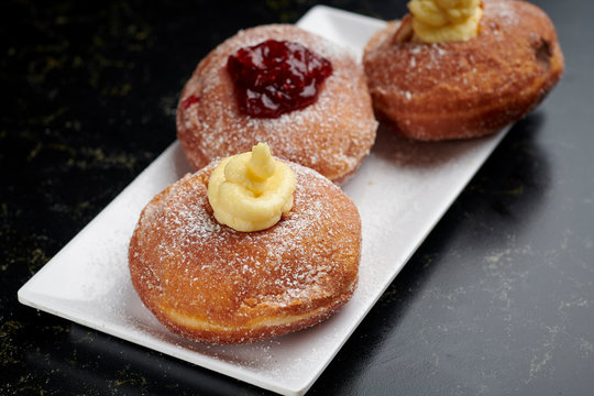 Three Italian bomboloni with cream and marmalade on a white plate