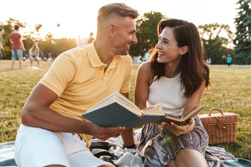 Portrait of joyful middle-aged couple man and woman smiling and reading books in summer park