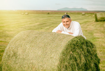 Naklejka na ściany i meble Happy man leaning on a green round hay bale in the countryside