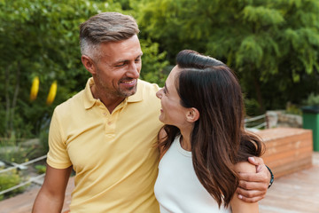 Portrait of smiling middle-aged couple looking at each other and hugging while walking in summer...