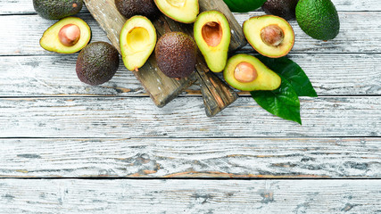 Avocado and green leaves on a white wooden background. Rustic style. Top view. Free space for your text.