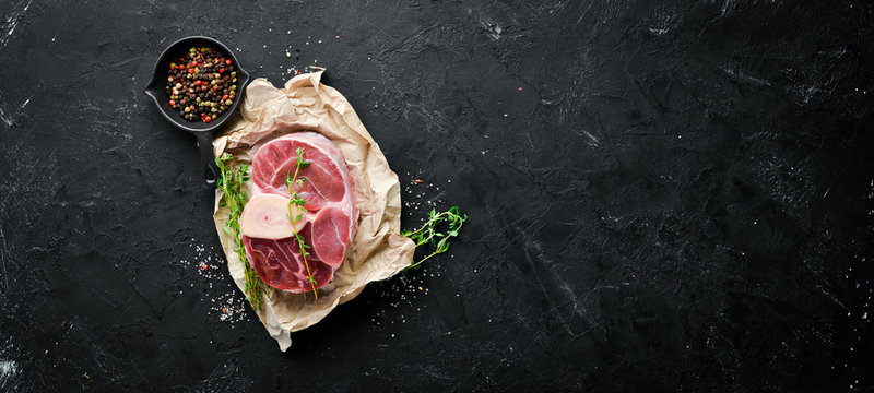 Raw fresh cross cut veal shank for making Osso Buco with spices and herbs on a black background. Top view. Free space for your text.