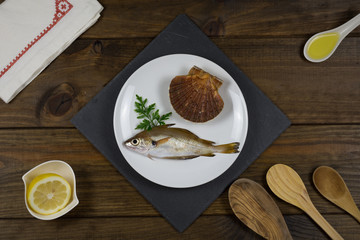 Pescado fresco sobre plato blanco en mesa de madera con utensilios de cocina.