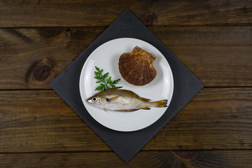 Pescado fresco sobre plato blanco en mesa de madera con utensilios de cocina.