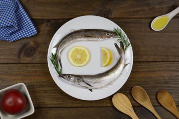Pescado fresco sobre plato blanco en mesa de madera con utensilios de cocina.