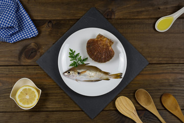 Pescado fresco sobre plato blanco en mesa de madera con utensilios de cocina.