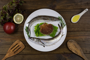 Pescado fresco sobre plato blanco en mesa de madera con utensilios de cocina.