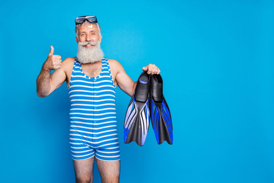 Portrait of retired grandfather with white hairstyle holding diving equipment wearing striped costume isolated over blue background