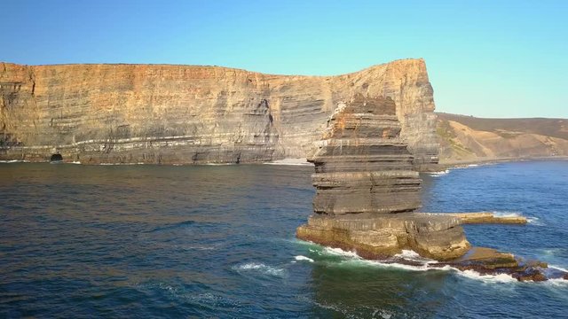 Aerial, orbit drone shot, around a large rock, on the Atlantic sea, near cliffs, at Arrifana Beach, on a sunny day, in Parque Natural do Sudoeste Alentejano e Costa Vicentina, in Portugal