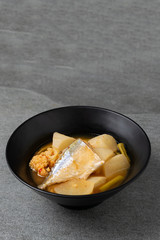 Sour curry with papaya and half fish in black bowl on the concrete table.