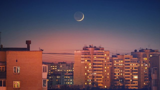 Beautiful waxing crescent moon setting behind city skyline buildings rooftops at night. Timelapse, 4K UHD.	