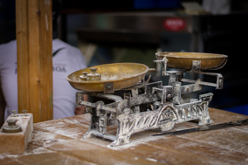 Báscula tradicional centenaria usada en panadería con marcas de harina sobre mesa de trabajo de madera.