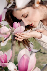 Attractive young woman enjoying her time outside in park with flowering tree in background.