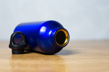 Blue thermo bottle with black lid lying on wooden table 