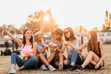 Female friends drinking beer and taking selfie at music festival