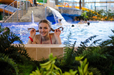 Young Caucasian girl with pigtails swimming in the pool in a closed winter water Park. Having a good time. He smiles and looks at the camera. Summer, holiday, Spa, weekend concept