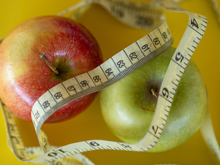 Bodegon mounted on a yellow background and composed of two apples and a tape to measure the waist.