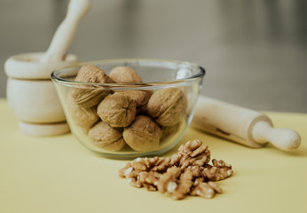Photograph from above of a still life mounted on a yellow background and composed of a kneader, a glass bowl and some nuts.