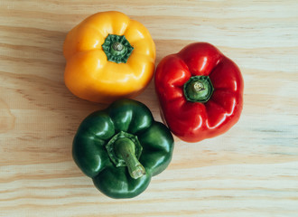 Foreground photograph from above of three colored peppers. Green, red and yellow .