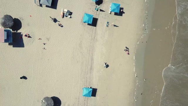Slow flyover a beach with umbrellas and waves caressing the sand