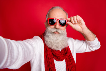 Fashion aged santa man making self photos wear sun specs knitted jumper isolated red background