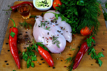 Chicken fillet is raw meat on a wooden board next to herbs and chilli pepper, oil and vinegar.  selective focus    