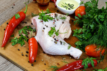   A quarter of the chicken is raw meat on a wooden board next to herbs and chili peppers, oil and vinegar.     selective focus 