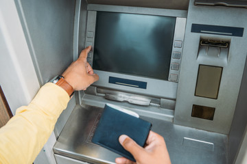 cropped view of mixed race man pressing button on atm machine and holding wallet