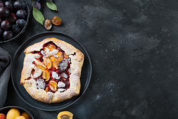 Homemade pie galette with plum and apricot on black table.