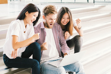 Happy excited successful three teenage while they use computer laptop in office