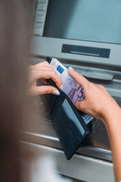 selective focus of woman putting money in wallet near atm machine