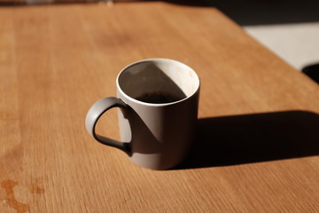 A half-finished coffee in a grey mug, casting a long shadow onto a coffee table one summer’s morning.