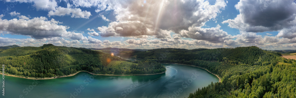 Wall mural Camera flies over the Hennesee near Meschede and takes a wide view picture. You can see a ship, hills and forests, sunbeams and lens flares. Gorgeous nature in the Sauerland. - Wall murals