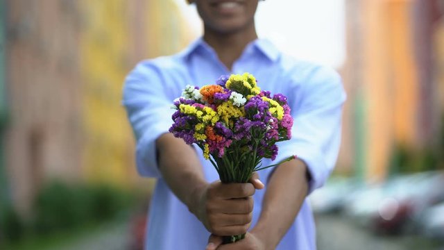 Mixed-race boy showing colored bouquet of flowers into camera, delivery, closeup