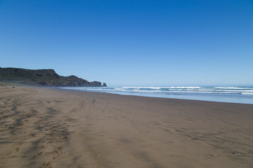 Fototapeta na wymiar Scorching hot day at Bethells Beach, west Auckland. Black sand gets hot. Stunning summers day at Te Henga with blue sky, minimal clouds, small white caps on the waves. Looking south toward caves.
