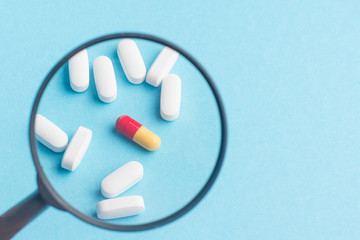 Concept - pharmaceutical testing, testing of medicines, magnifying glass, tablets on a blue...