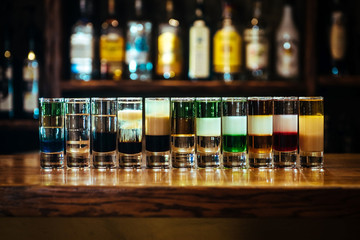 Different alcoholic cocktails. Multilayer short drink on a wooden table in a bar on the background...