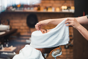 Barber covers the face of a man with a hot towel. Shaving the beard with hot and cold compresses in...