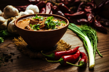 Kharcho soup with fresh parsley on a wooden background with fresh vegetables onions and garlic. Traditional georgian meat soup
