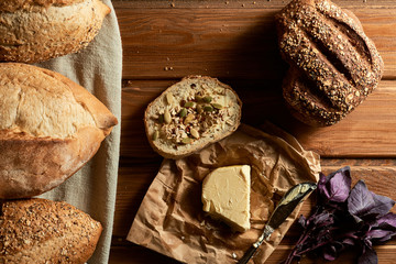 A slice of wheat bread and butter sprinkled with various grains, homemade butter, basil leaves and...