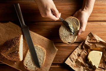 Man's hands grease an old knife with butter on a slice of wheat bread. Homemade butter, sliced ​​fresh bread and a knife for slicing bread on a rustic table. Wood background.
