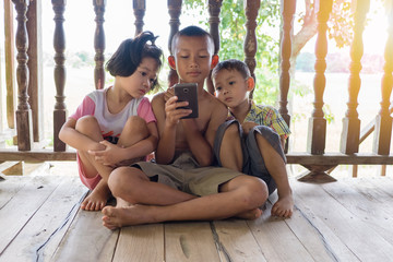 Three children sit and watch the smartphone happily. young boys and girls with cellphone communication. on the terrace of their house. to see today's children addictive technology.
