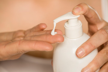 Woman applying skin cream from the bottle with pump