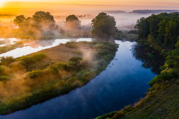 Fototapeta na wymiar Amazing rural landscape. Blue river flows in countryside. Thick fog in golden sun rays